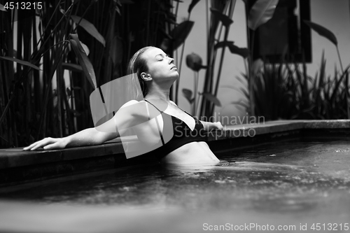Image of Sensual young woman relaxing in outdoor spa infinity swimming pool surrounded with lush tropical greenery of Ubud, Bali. Black and white image.