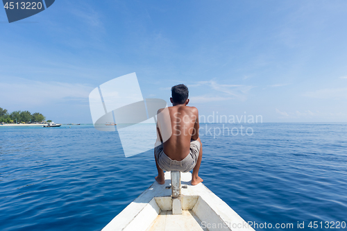 Image of Local Sporty Guy Sitting Topless at the Bow of Traditional White Wooden Sail Boat, Looking At Beautiful Blue Sea of Gili Islands near Bali, Indonesia