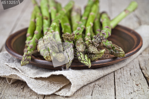 Image of Fresh raw garden asparagus closeup on brown ceramic plate and li