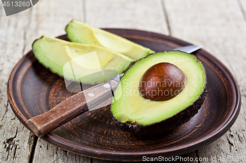 Image of Fresh organic avocado on ceramic plate and knife on rustic woode