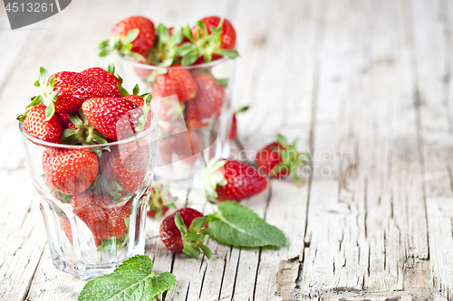 Image of Organic red strawberries in glass and mint leaves on rustic wood