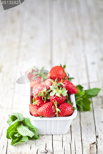 Image of Fresh red strawberries in white bowl and mint leaves on rustic w