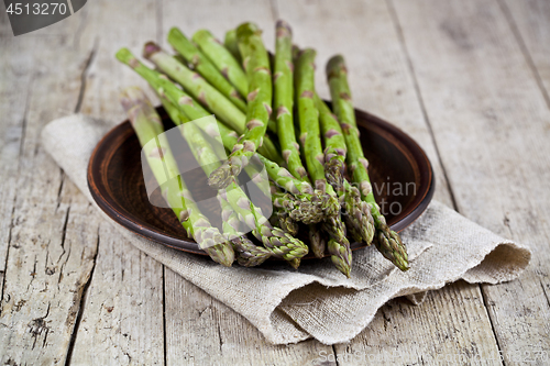 Image of Fresh raw garden asparagus closeup on brown ceramic plate and li