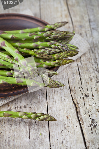 Image of Fresh raw garden asparagus closeup on brown ceramic plate and li