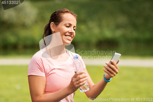 Image of woman with smartphone drinking water in park