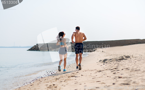 Image of couple in sports clothes running along on beach