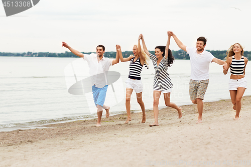 Image of friends in striped clothes running along beach