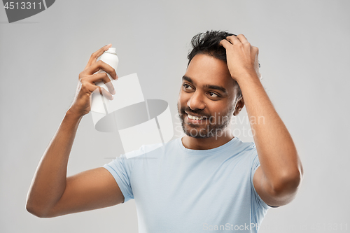 Image of smiling indian man applying hair spray over gray