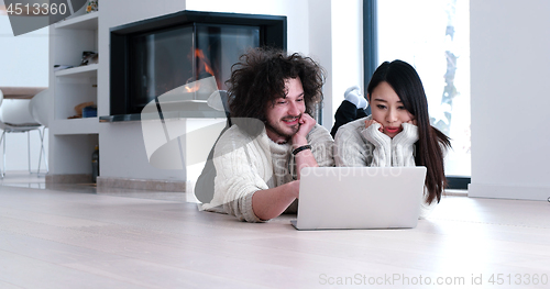 Image of young multiethnic couple using a laptop on the floor