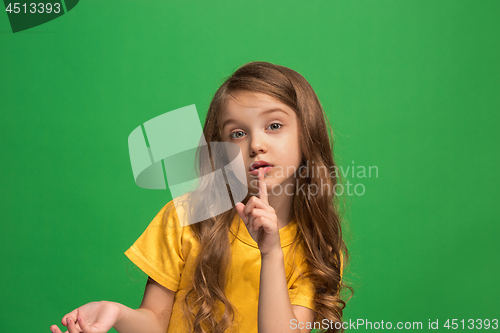 Image of The young teen girl whispering a secret behind her hand over green background