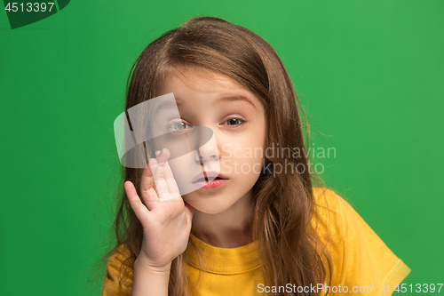 Image of The young teen girl whispering a secret behind her hand over green background