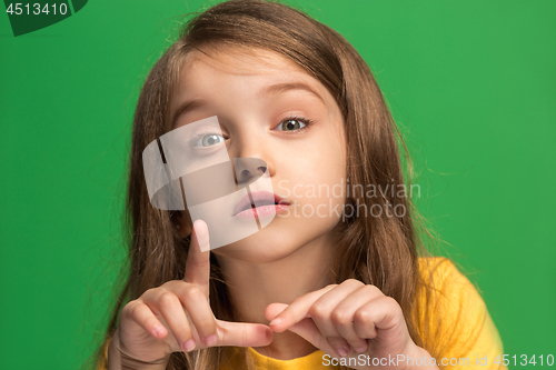 Image of The young teen girl whispering a secret behind her hand over green background