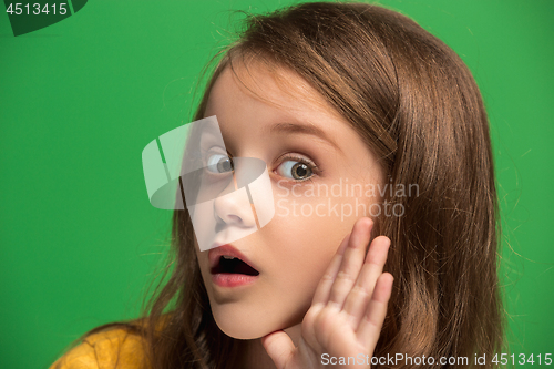 Image of The young teen girl whispering a secret behind her hand over green background