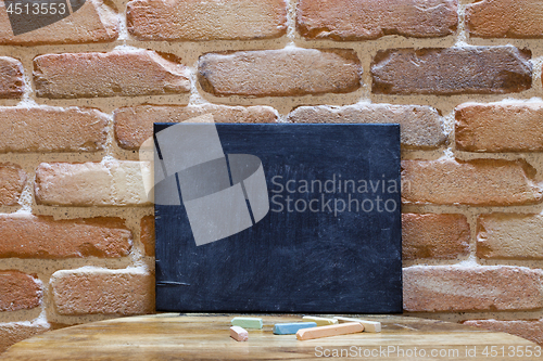 Image of Blank blackboard on wooden table at brick wall.