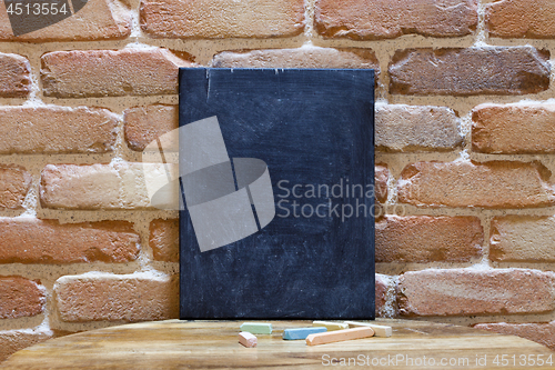 Image of Blank blackboard on wooden table at brick wall.