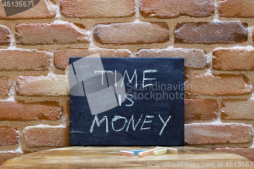 Image of Black board with the phrase "Time is Money" drown by hand on woo