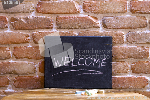 Image of Black board with the word WELCOME drown by hand on wooden table 