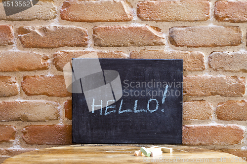 Image of Black board with the word HELLO! drown by hand on wooden table o