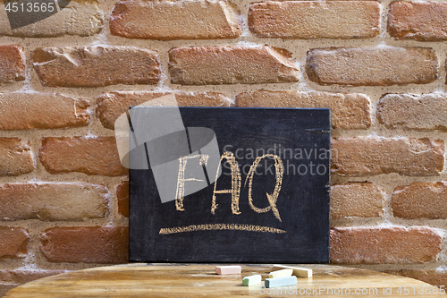 Image of Black board with the word FAQ drown by hand on wooden table on b