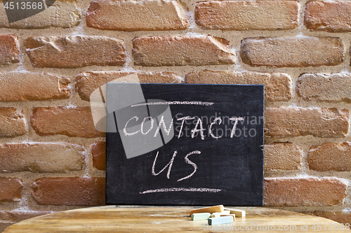 Image of Black board with the phrase CONTACT US drown by hand on wooden t