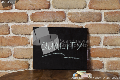 Image of Chalk board with the word QUALITY drown by hand on wooden table 