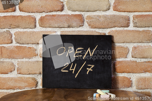 Image of Black chalkboard with the phrase OPEN 24/7 drown by hand on wood