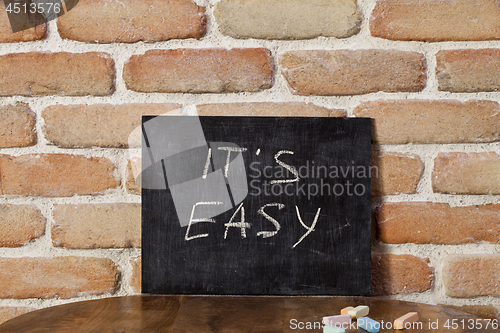 Image of Black board with the phrase IT'S EASY drown by hand on wooden ta