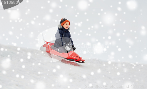 Image of happy boy sliding on sled down snow hill in winter