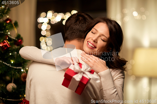 Image of happy couple with christmas gift hugging at home