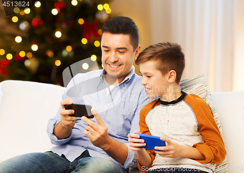 Image of happy father and son with smartphones on christmas