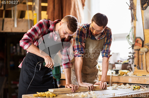 Image of carpenters with drill drilling board at workshop