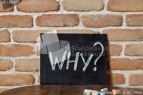 Image of Black board with the word WHY? drown by hand on wooden table on 