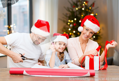 Image of happy family wrapping christmas gifts at home