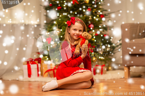 Image of girl in red dress hugging teddy bear at home