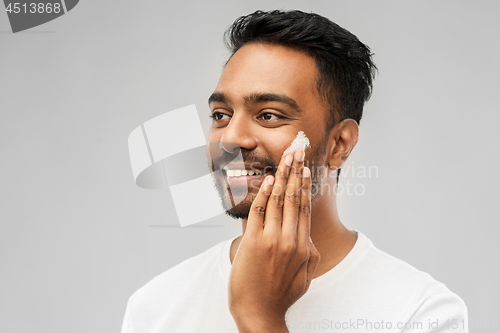 Image of happy indian man applying cream to face