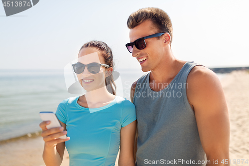 Image of couple in sports clothes with smartphones on beach