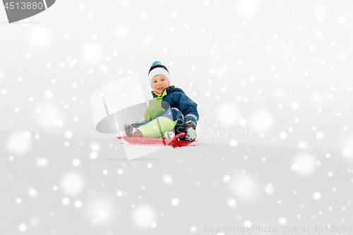 Image of happy boy sliding on sled down snow hill in winter