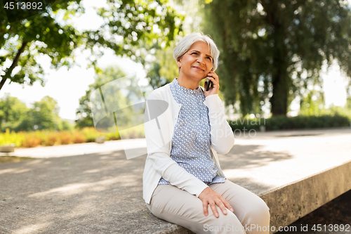 Image of happy senior woman calling on smartphone in summer