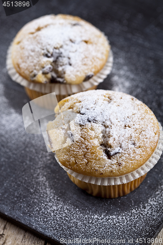 Image of Two fresh homemade muffins with sugar powder closeup on black bo