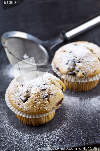 Image of Two fresh homemade muffins with sugar powder and metal strainer 