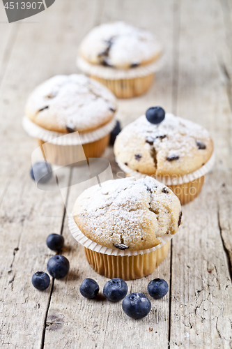 Image of Four fresh homemade muffins with blueberries on rustic wooden ta