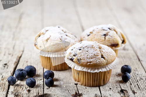 Image of Three fresh baked homemade muffins with blueberries on rustic wo