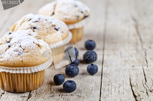Image of Three fresh baked homemade muffins with blueberries on rustic wo