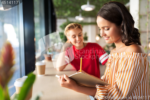 Image of woman with friend at cafe writing to notebook