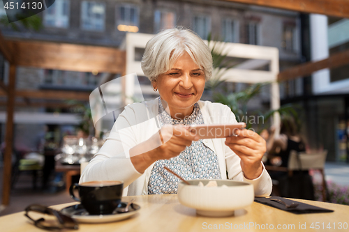 Image of senior woman photographing food at street cafe