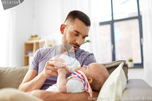 Image of father feeding baby daughter from bottle at home