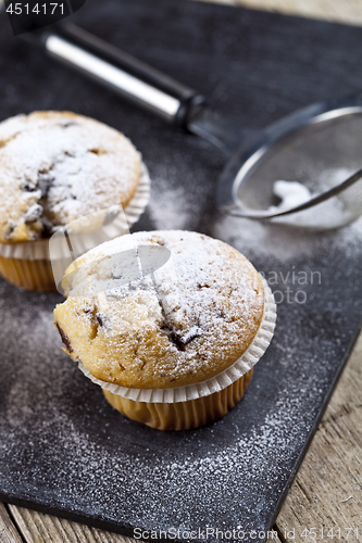 Image of Two fresh homemade muffins with sugar powder and metal strainer 
