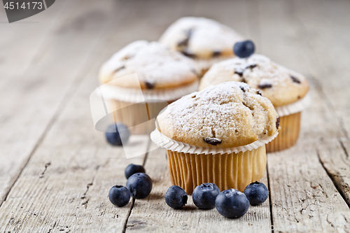 Image of Four fresh homemade muffins with blueberries on rustic wooden ta