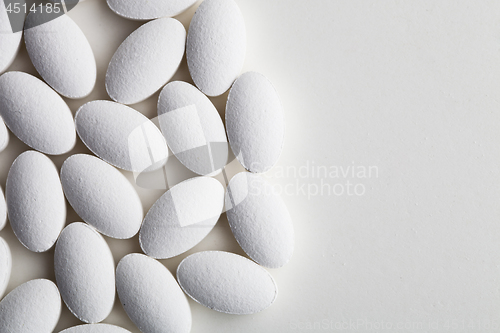 Image of Pile of white drug pills laying on white background. 