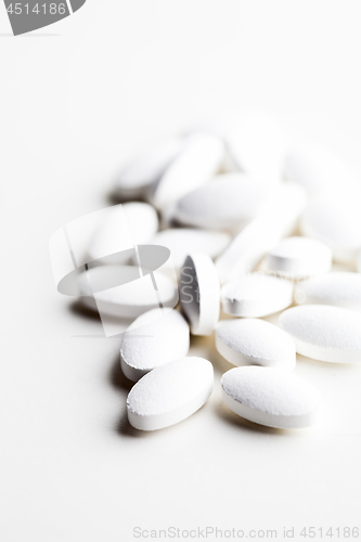 Image of Pile of white drug pills laying on white background.